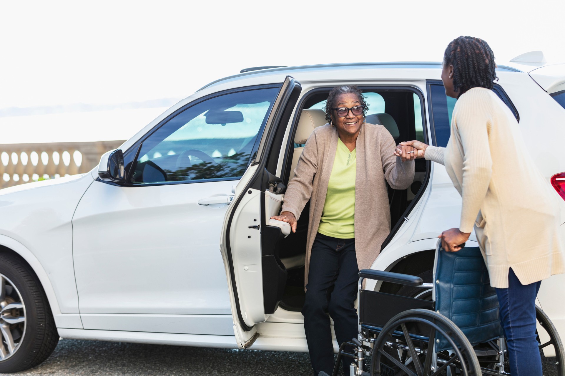 Senior woman exits car into wheelchair, caregiver helps
